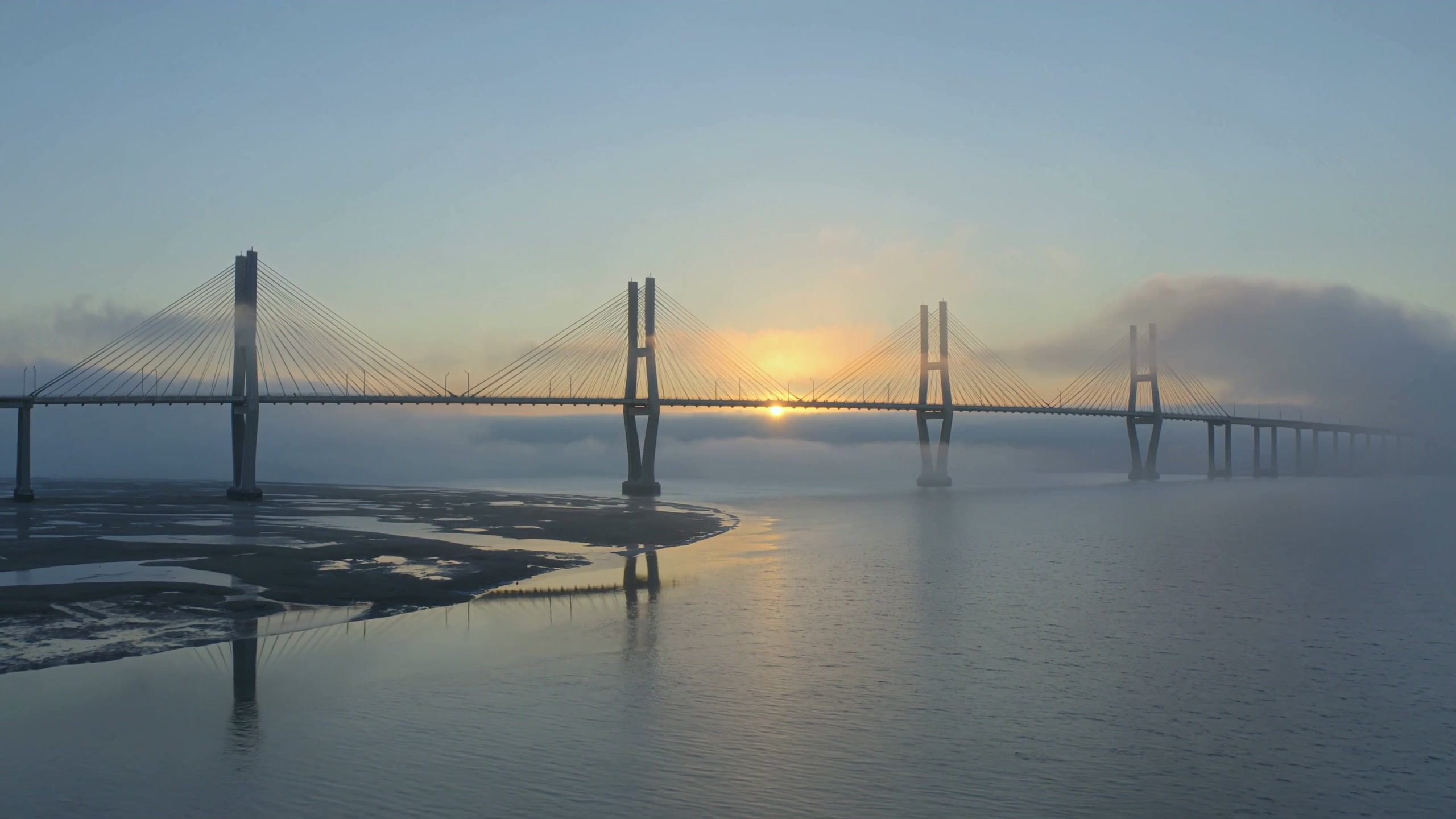 A modern cable-stayed bridge with slender white towers rising from dawn mist over a wide firth, the low sun breaking through fog banks.